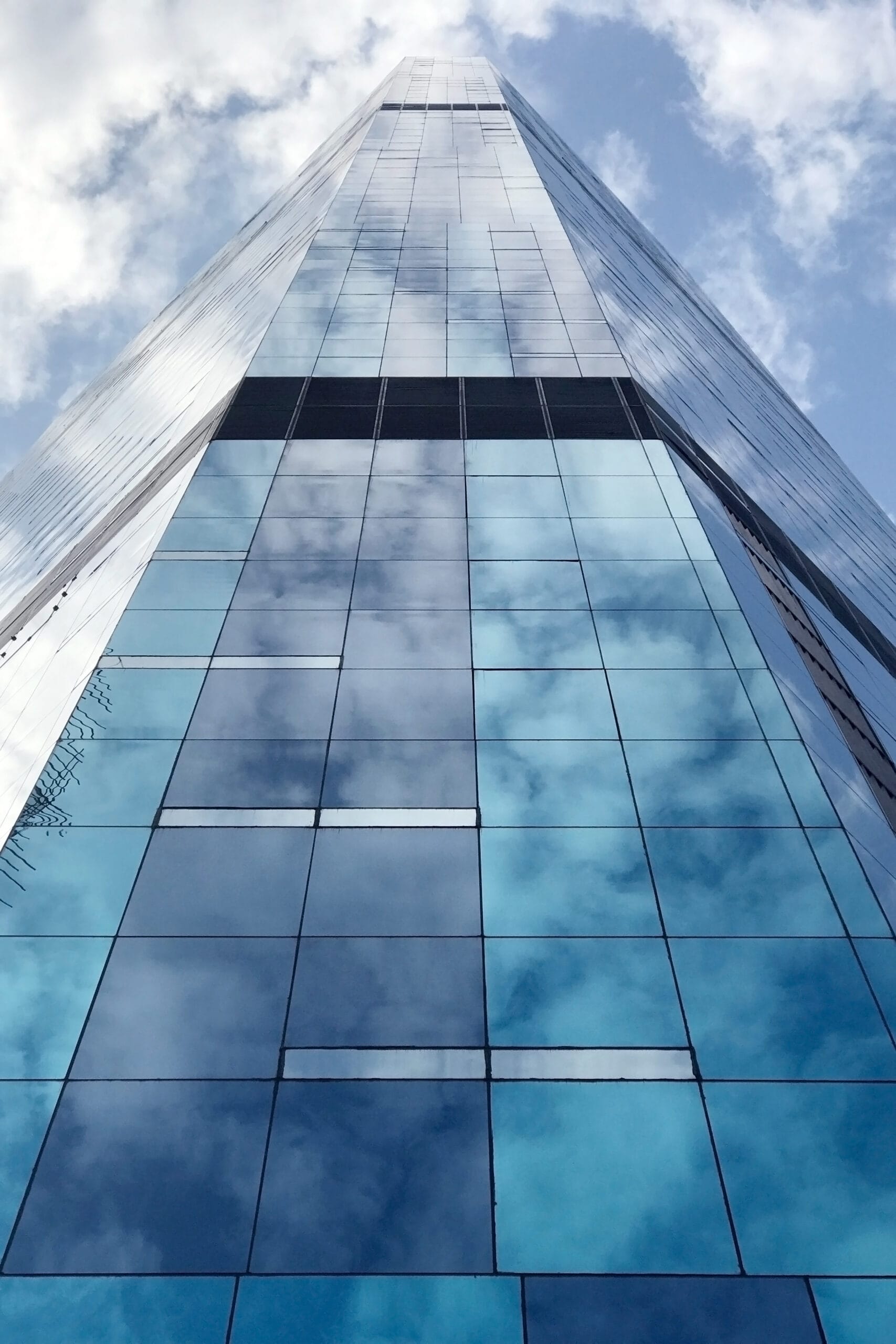 Vertical low angle shot of a commercial building in the downtown district with the cloud reflections